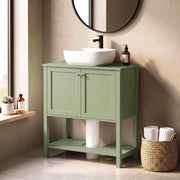 Green under sink cabinet beside a window with a vessel sink and towels on the lower shelf