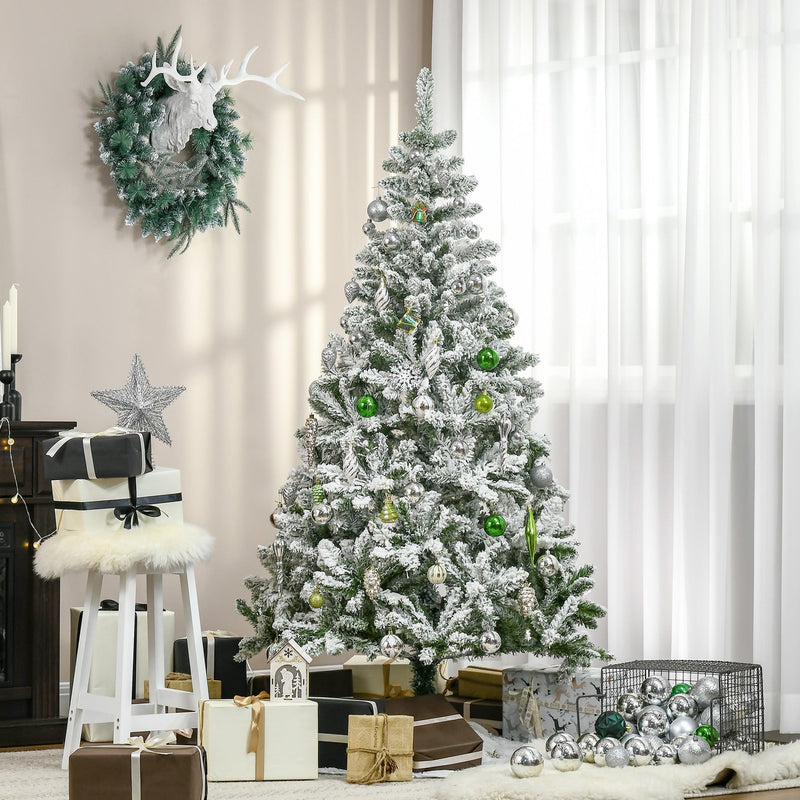 Flocked tree decorated with baubles and a wreath in a living room beside a window