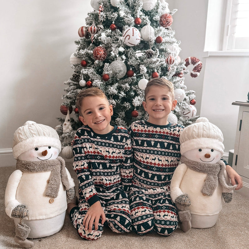 Two children sitting in front of a decorated flocked tree with snowman toys