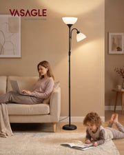 Uplighter floor lamp lit in a living room beside a woman on a sofa and a child reading on the rug