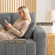 Woman leaning on the wide armrest and pillow of a grey velvet sofa