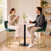 Couple chatting on dark green velvet bar stools at a small round table