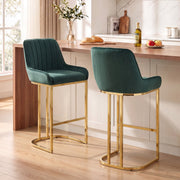 Two dark green velvet bar stools with gold legs at a wooden kitchen counter