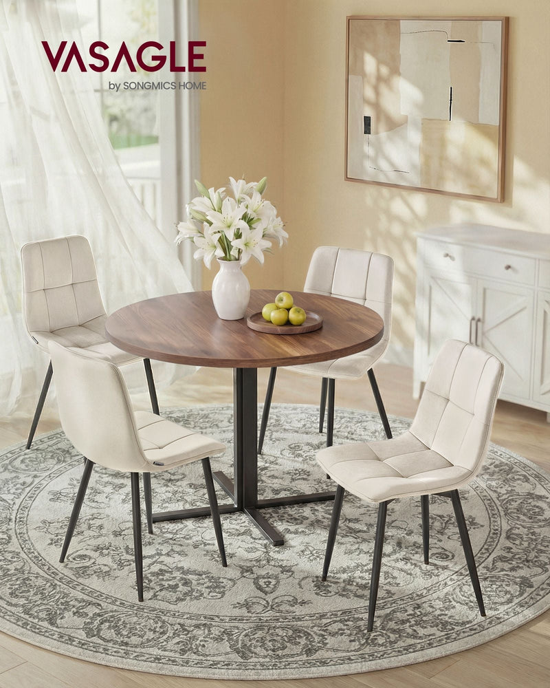 Four beige velvet dining chairs around a round wooden table in a bright dining room