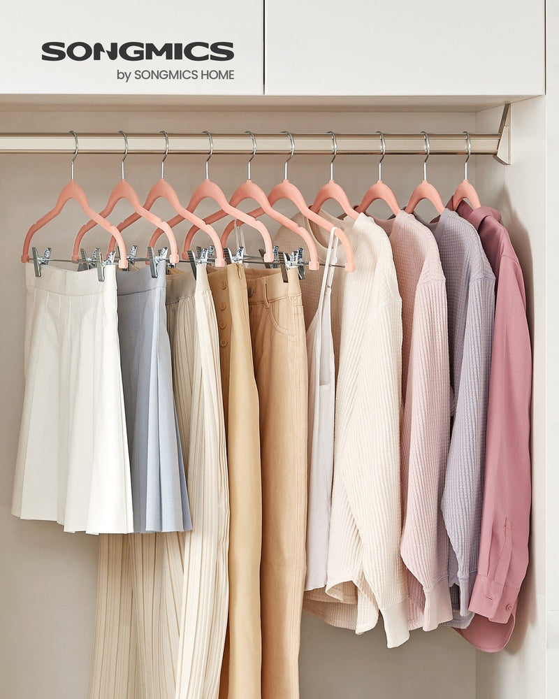 Light pink velvet clip hangers holding skirts and trousers on a wardrobe rail