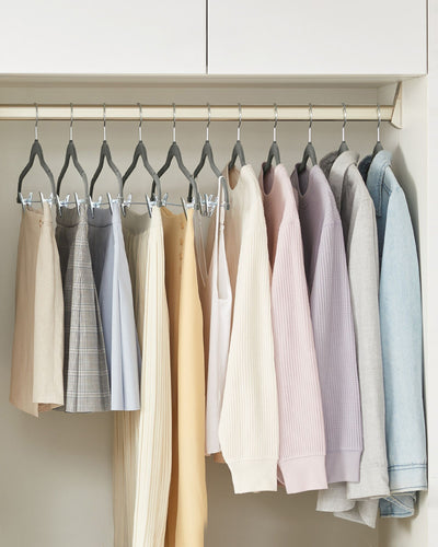 Grey velvet hangers holding trousers and skirts on a wardrobe rail
