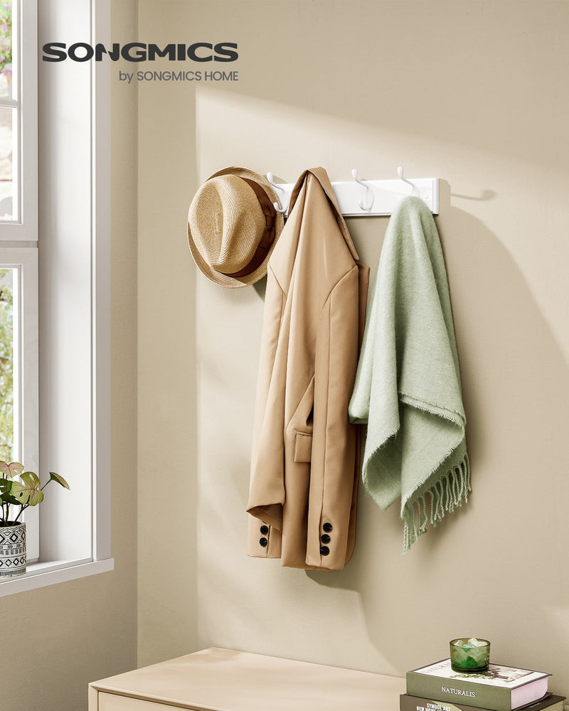 White coat rack mounted on a hallway wall holding a straw hat, camel coat and green throw