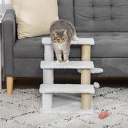 Tabby cat standing on the middle step of the cat stairs in front of a grey sofa