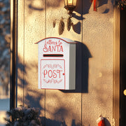 White Santa postbox mounted on a textured wall beside a porch lantern at dusk