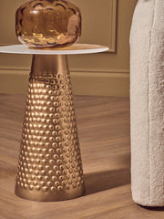 Round gold side table used as a bedside table next to a bed