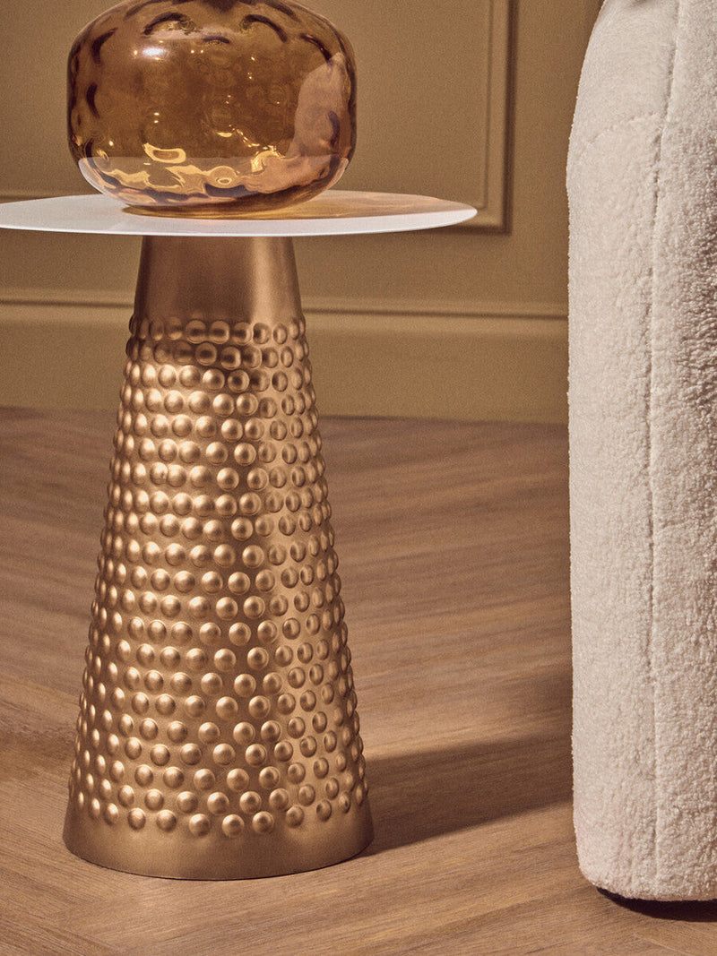 Round gold side table used as a bedside table next to a bed