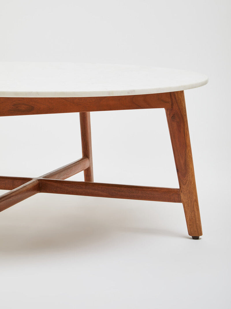 Low-angle room view of the marble coffee table and its acacia legs