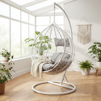 White rattan effect hanging chair styled in a bright sunroom setting