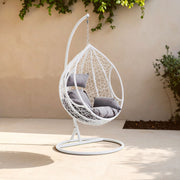 White rattan effect hanging chair with grey cushions styled in a living room