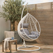 White rattan hanging chair shown in an outdoor patio setting