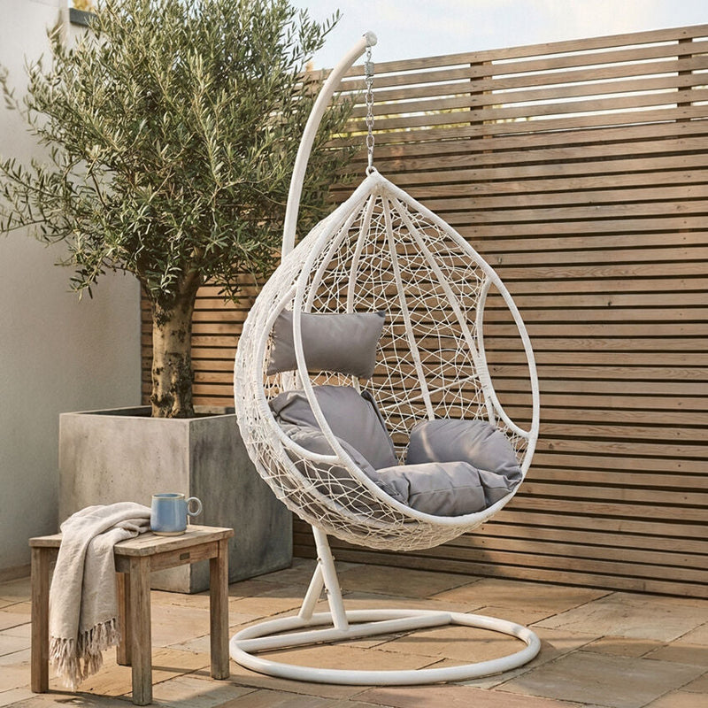 White rattan hanging chair shown in an outdoor patio setting