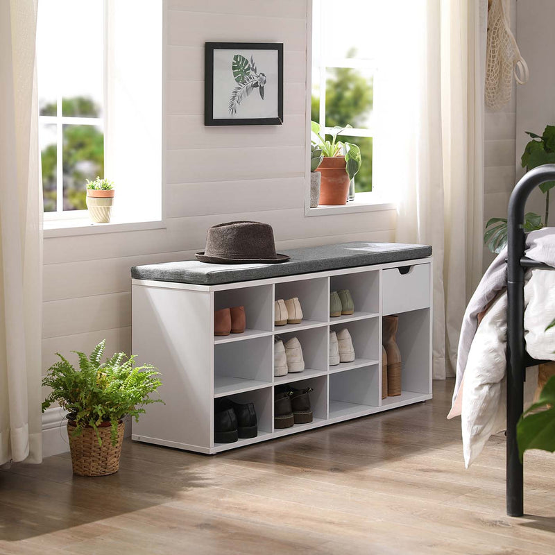 The shoe bench against a bedroom wall on wooden flooring, with a hat resting on the grey seat