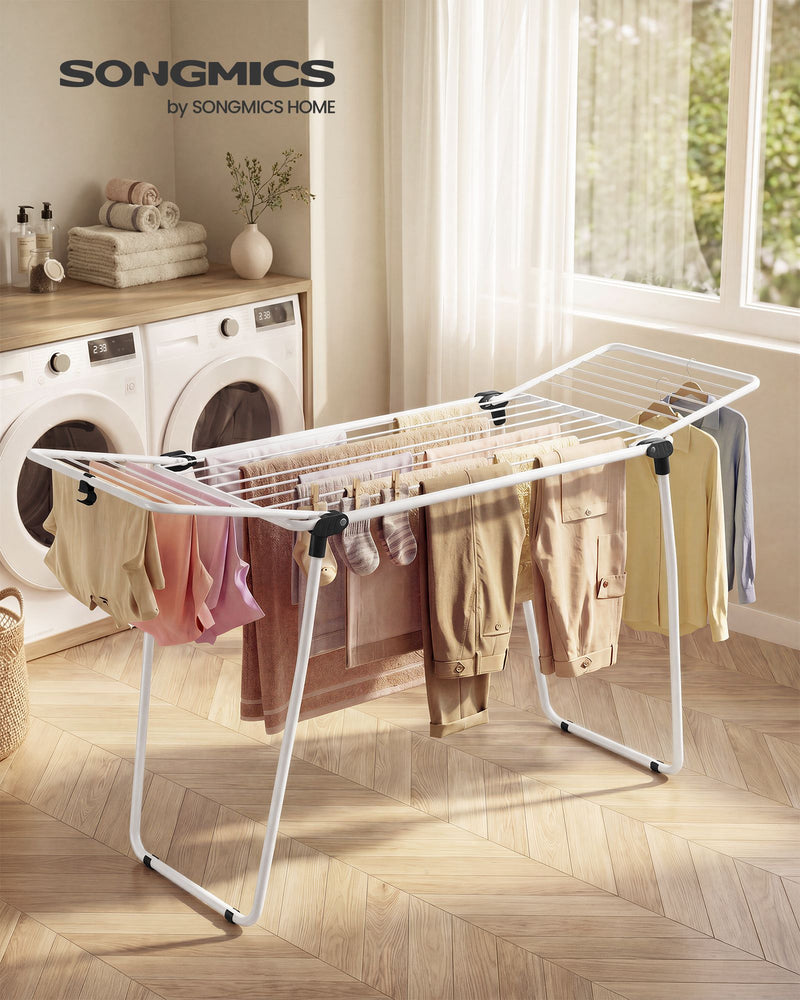 Winged airer loaded with trousers, towels and shirts in a laundry room beside washing machines