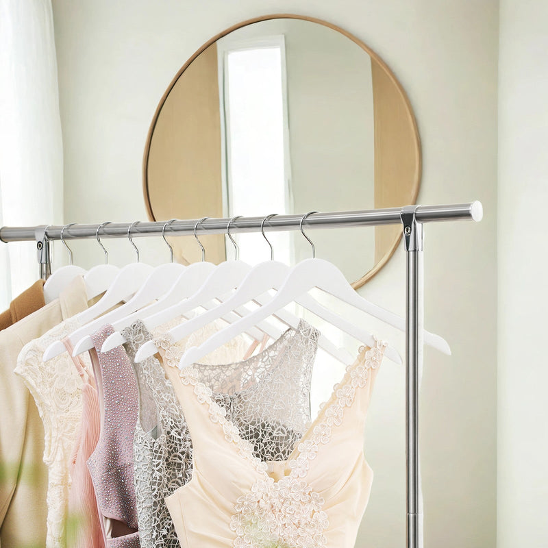 White wood hangers holding dresses and tops on a clothing rail below a mirror