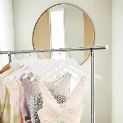 White wood hangers holding dresses and tops on a clothing rail below a mirror