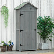 Grey sentry box shed standing closed against a white fence with a hanging basket and potted tree
