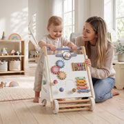 Mother helping a baby push the wooden baby walker across a living room floor