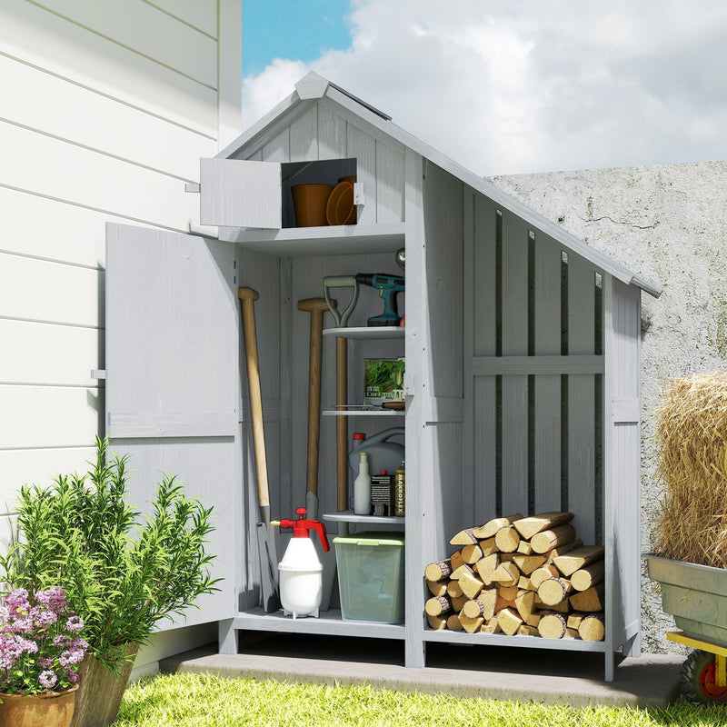 Grey wooden garden shed against a house wall with the door open and firewood stacked in the side rack