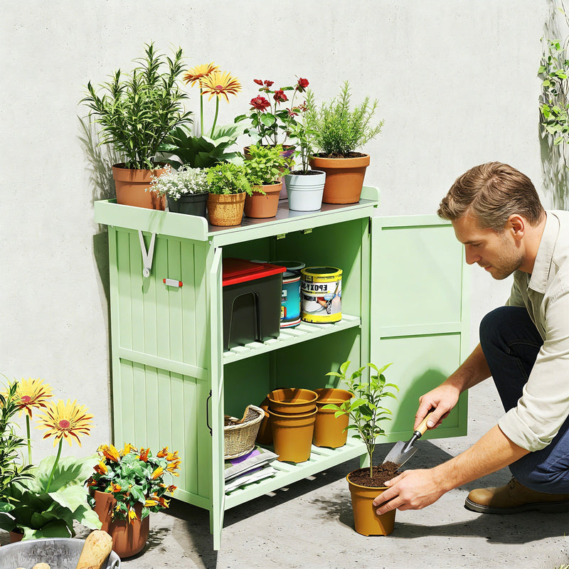 Man kneeling beside the light green shed planting into pots, with flowers arranged on the worktop