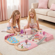 Two girls building the pink princess castle train set on a living room rug