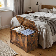 Storage bench with lid open at the foot of a bed, showing folded clothes and a cushion inside
