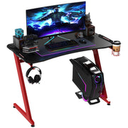 Red-framed Z-shaped gaming desk with a monitor, headphones on the hook and a PC tower beside it