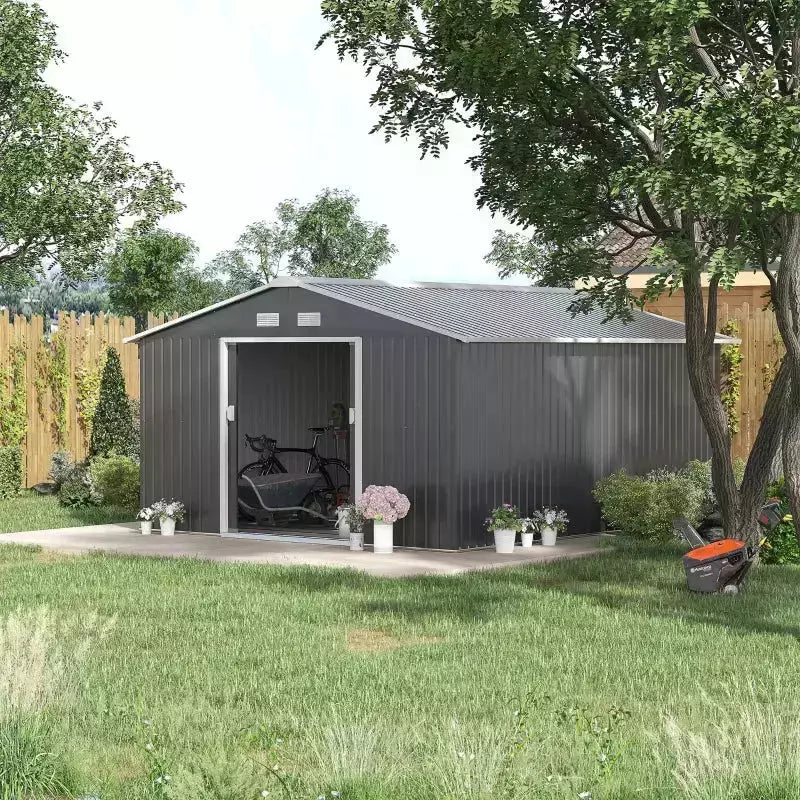 Dark grey metal garden shed on a patio with sliding doors open and a mower nearby